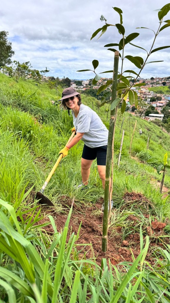Voluntária do Bora Plantar coroando muda em encosta com vista da cidade